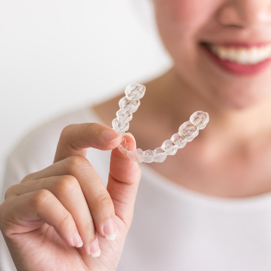 A smiling woman holding invisalign or invisible braces, orthodontic equipment