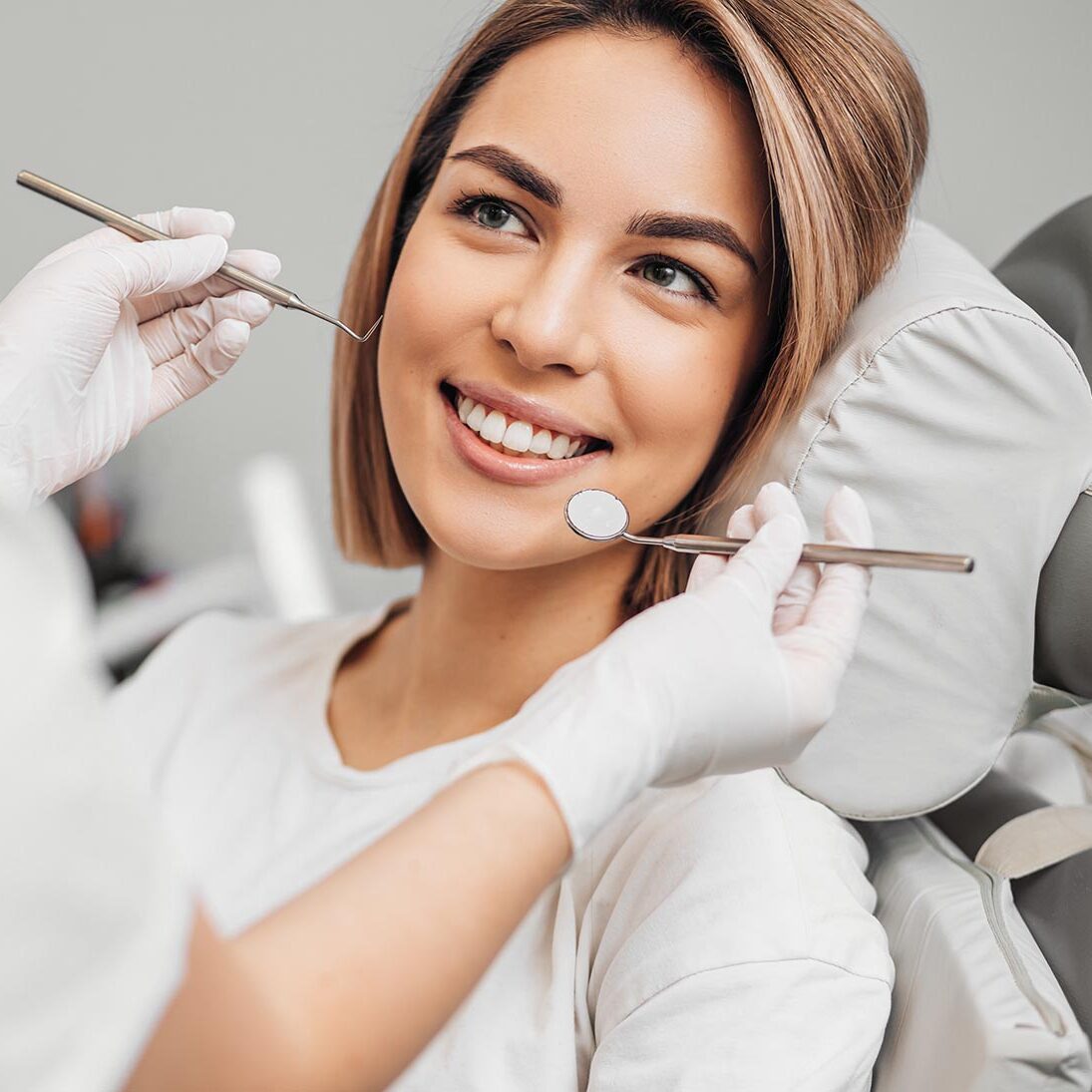 good-looking woman with short hair sit in dental office and look at doctor with confidence, she has perfect smile. professional doctor of clinic use special sterilized medical instruments